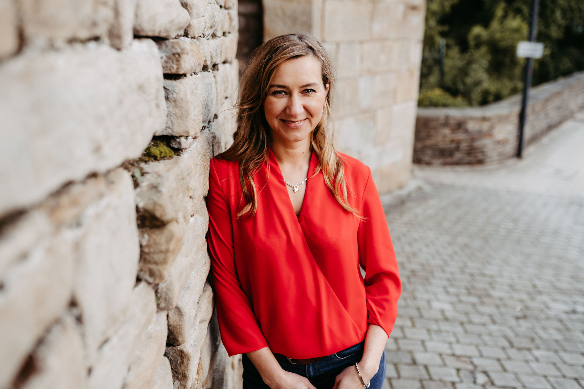 A young woman in a red blouse exhibits confidence with a relaxed pose against a stone background.
Karriere & Hypnose-Coaching 